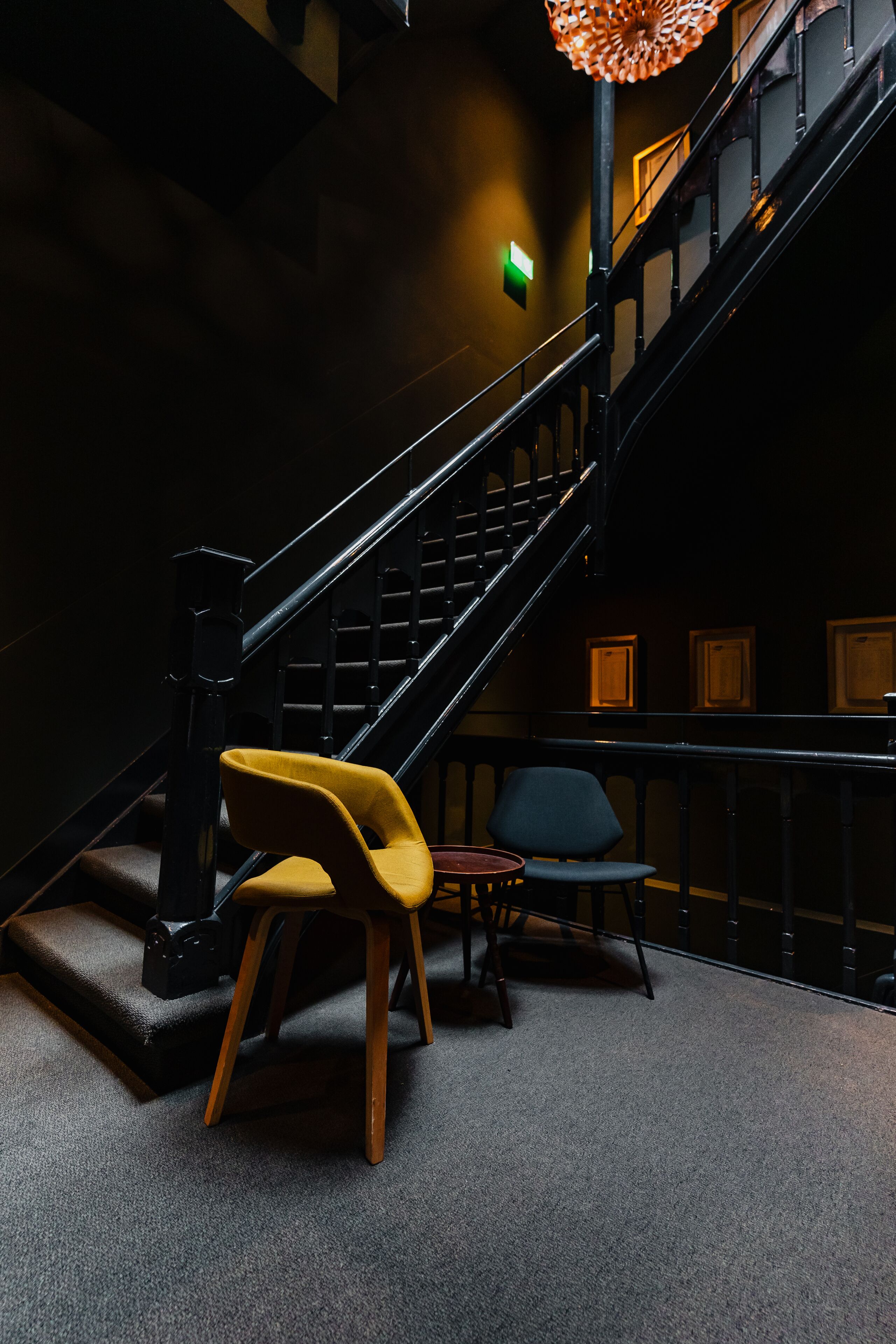 A staircase with a black railing, a yellow chair, and a blue chair in a dimly lit room.