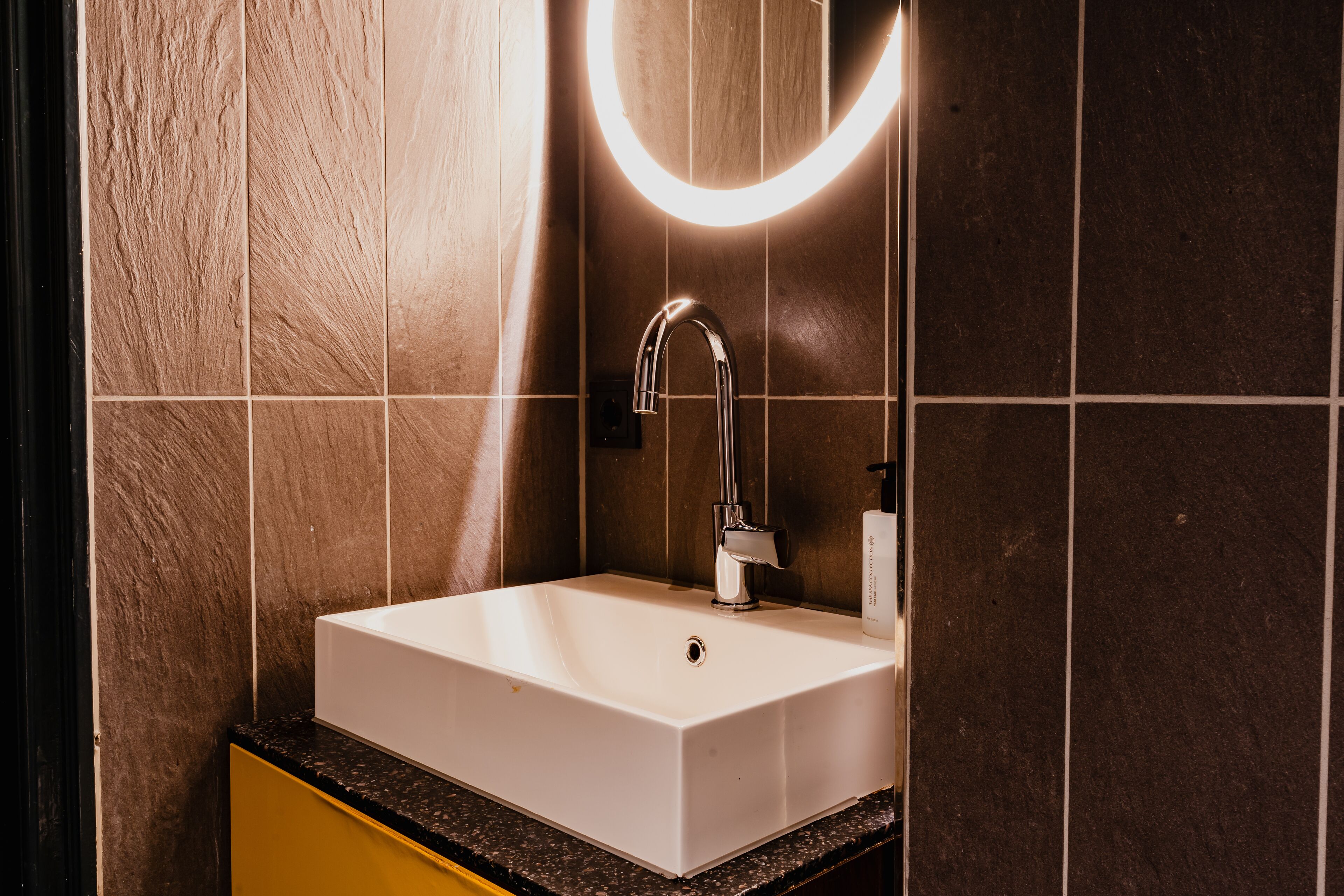 A bathroom with a white sink, a mirror with a light, and a yellow cabinet.