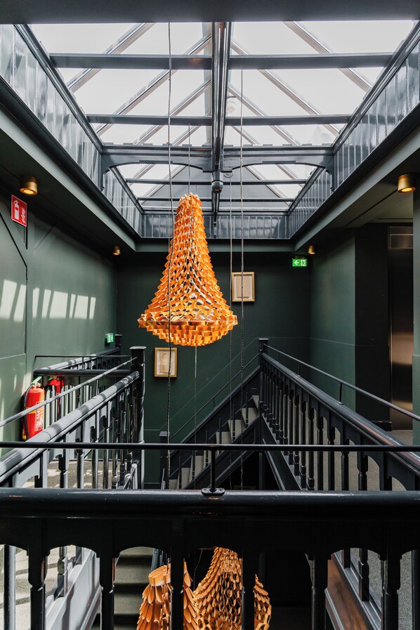 A modern interior with a glass ceiling, metal railings, and a unique orange hanging light fixture. - De Jonker Urban Studio's & Suites (Amsterdam)