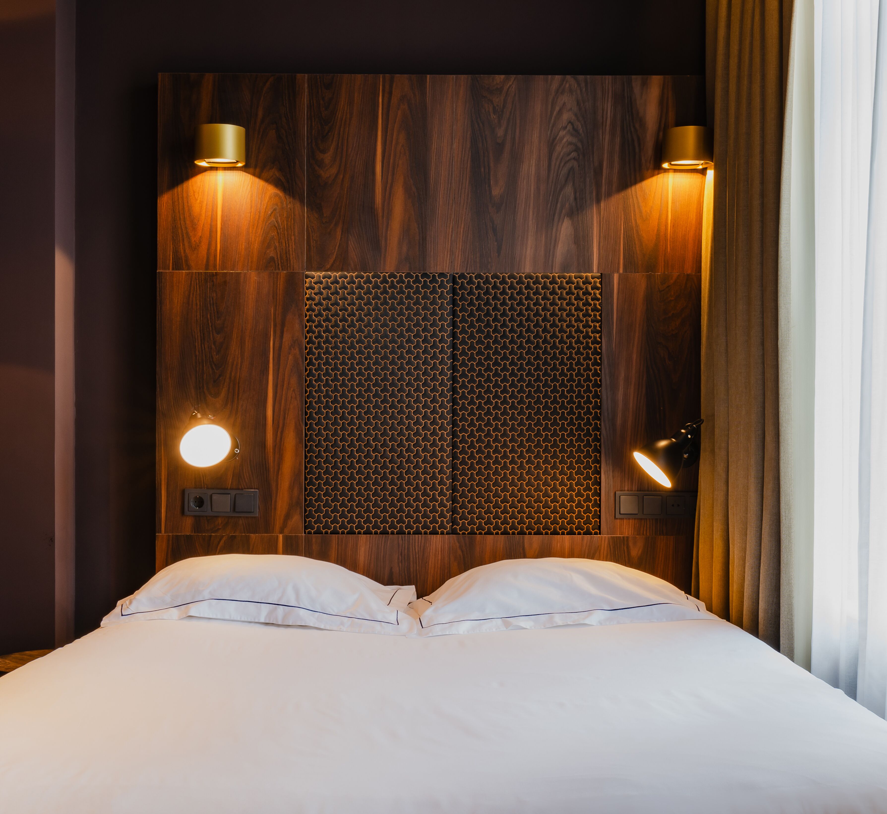 A hotel room with a wooden headboard, two bedside lamps, and a bed with white linens.