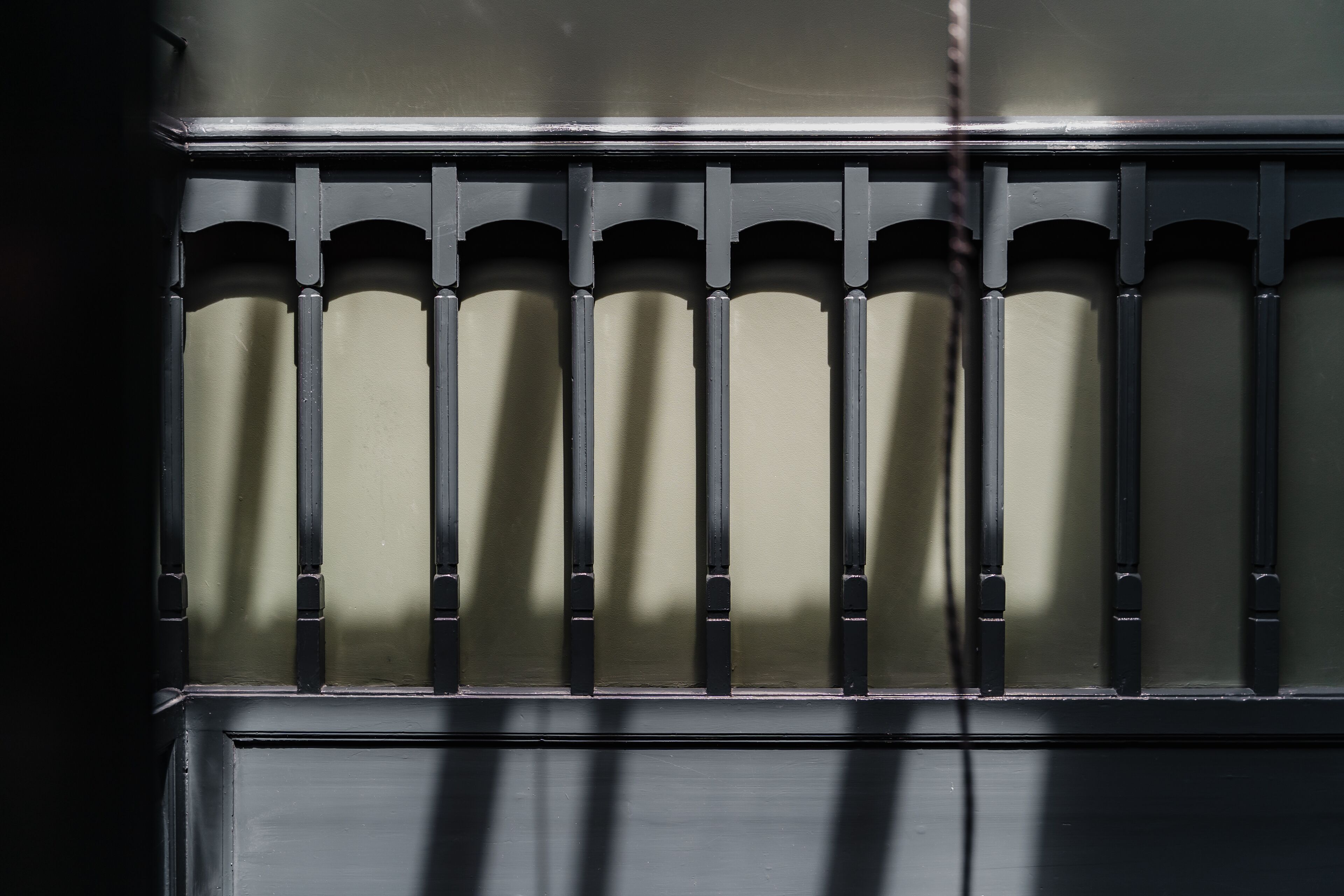 Un gros plan d’une grille en métal noir avec des barreaux verticaux, sur un fond beige.