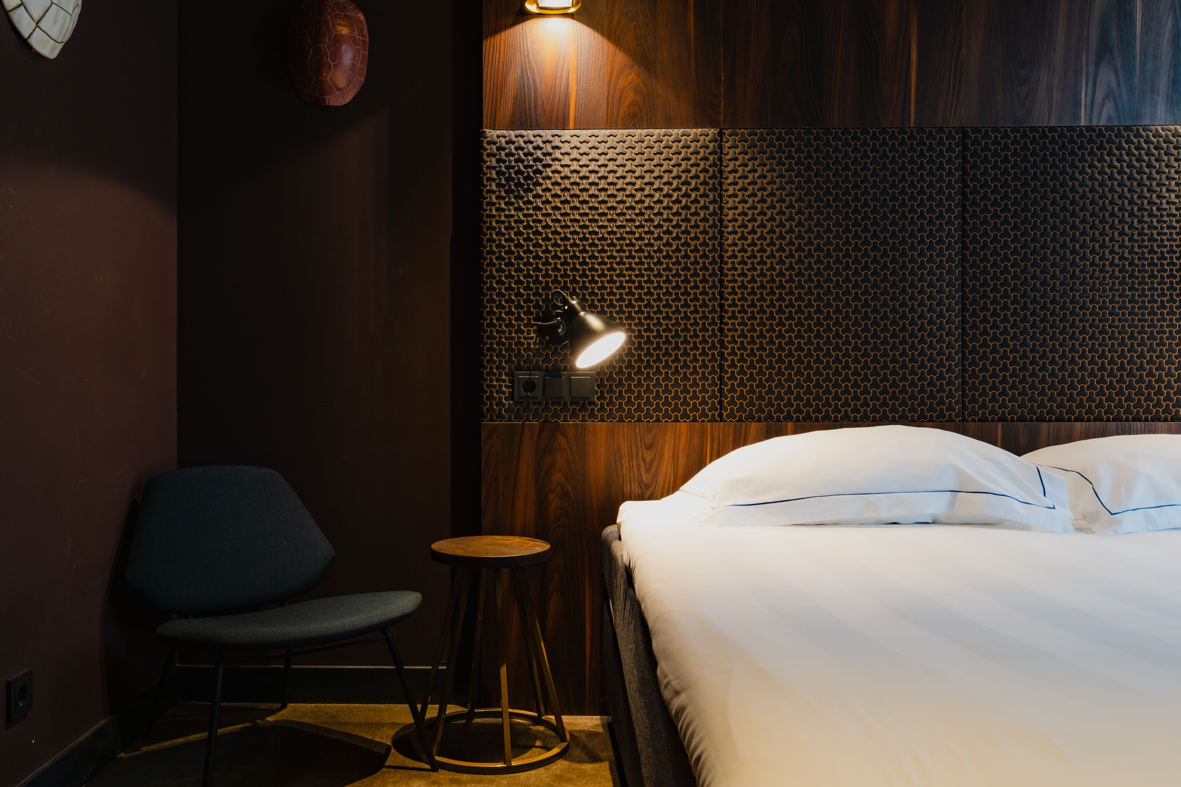 Een hotelkamer met een bed, een stoel, een klein rond tafeltje en een wandlamp.
