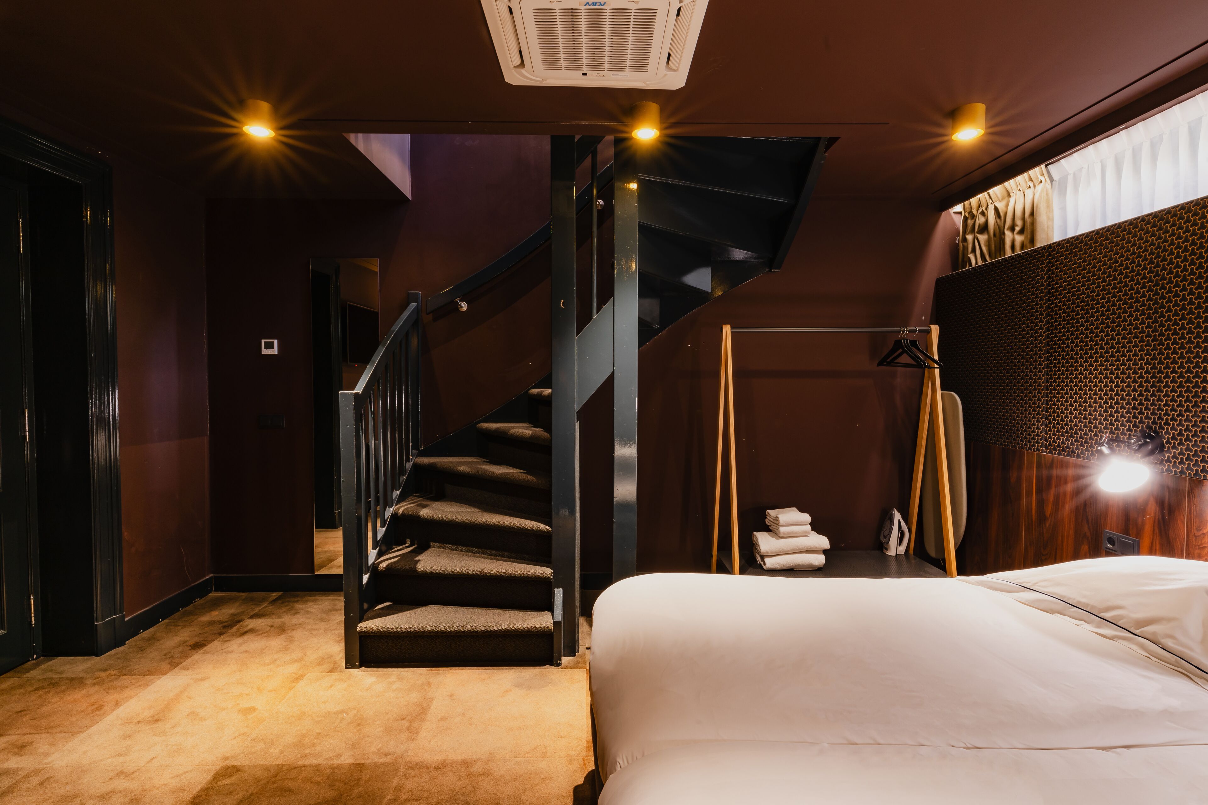 Una habitación de hotel moderna con una escalera, una cama y un gran ventanal con cortinas.