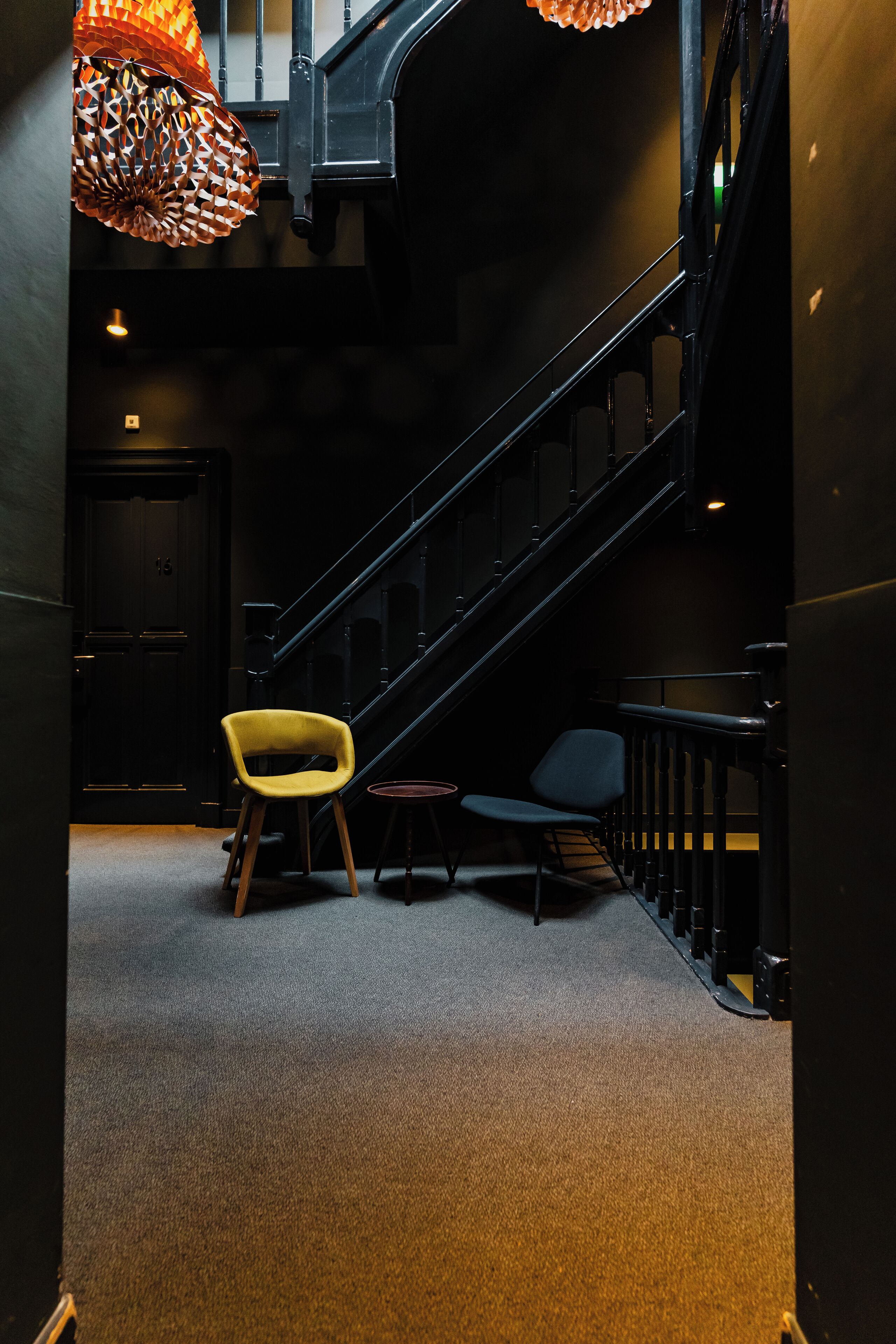 A staircase with a handrail, a yellow chair, and a blue chair in a dimly lit hallway.