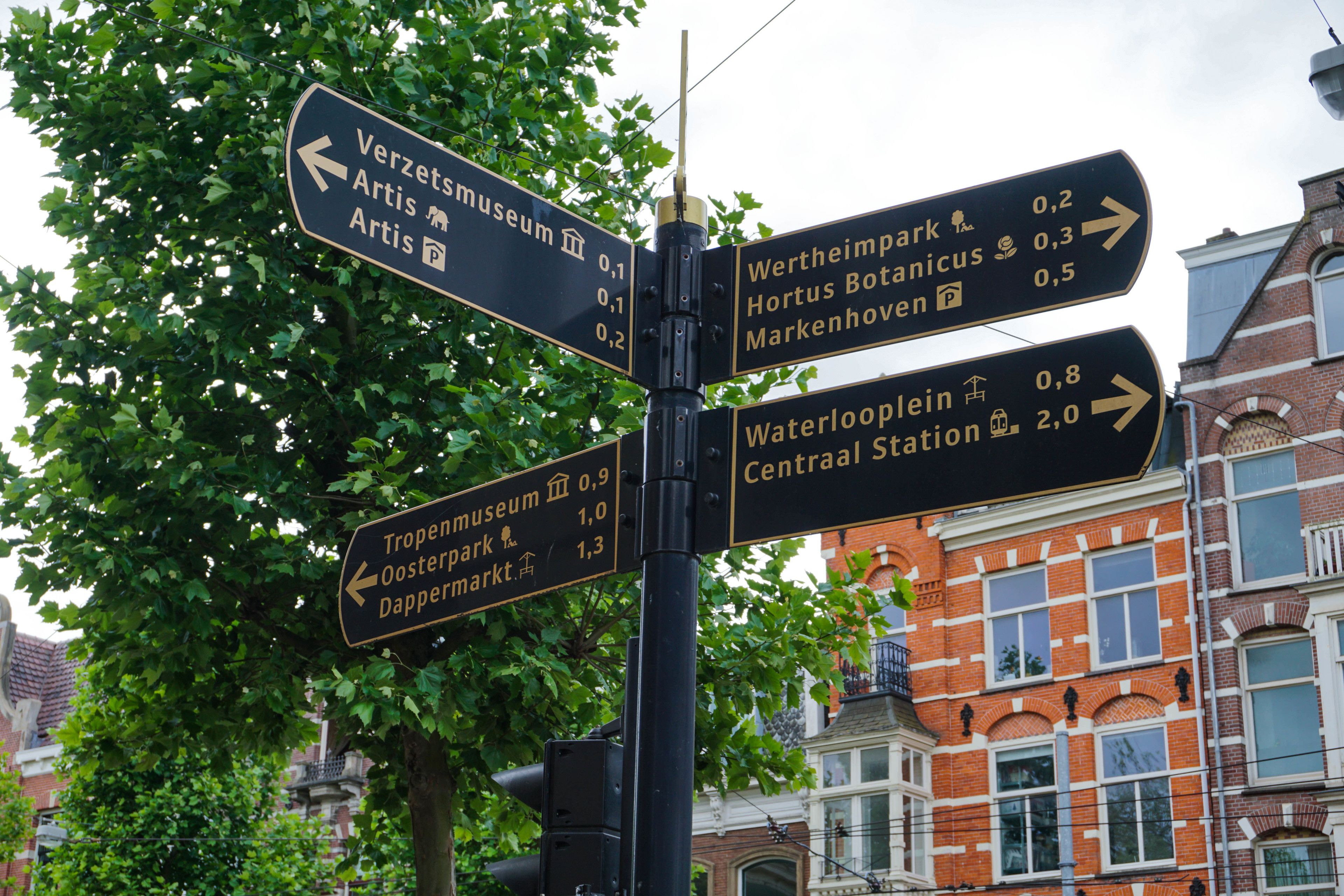 A directional signpost with multiple arrows pointing to various destinations such as Verzetsmuseum, Hortus Botanicus, and Waterlooplein.