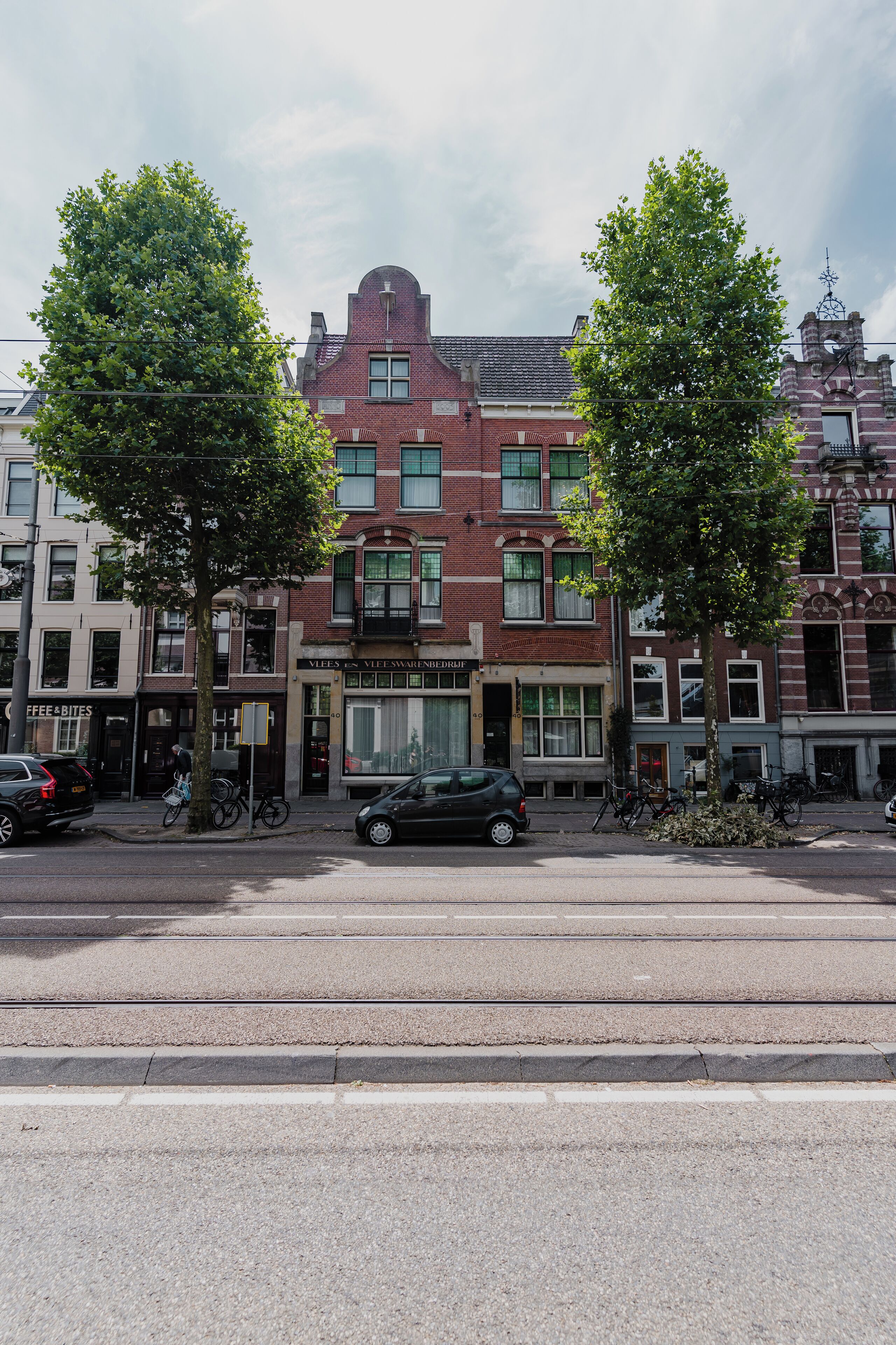 Une vue de rue avec une rangée de bâtiments, dont un magasin dont l’enseigne indique : « VEE’S VEEWARENDEELIJF ».