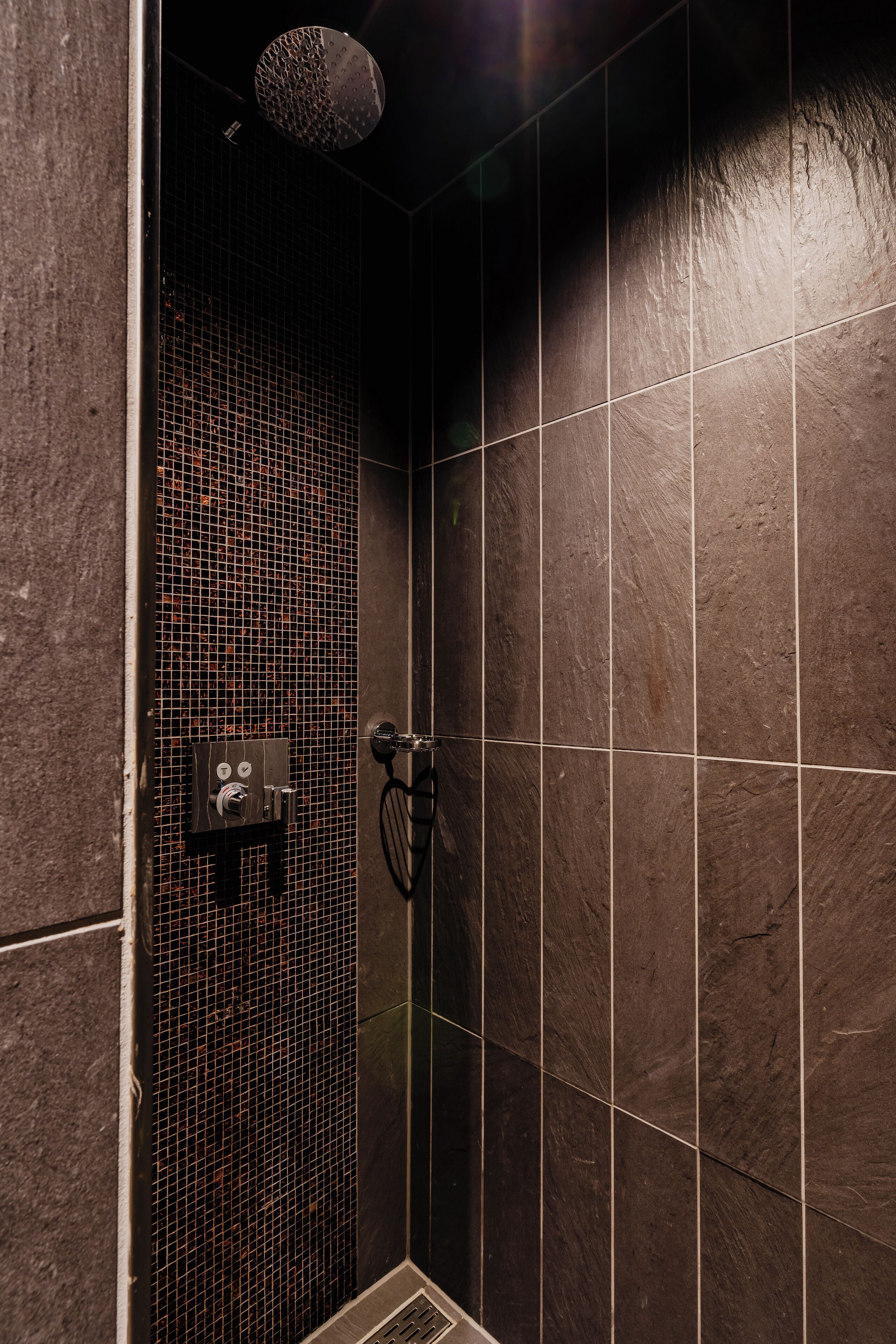 A shower area with tiled walls, a showerhead, and a control panel.