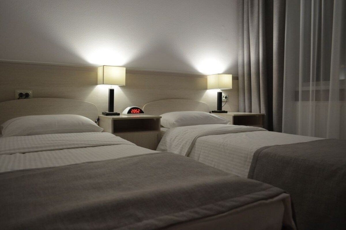 A hotel room with two beds, each with a bedside table and lamp.