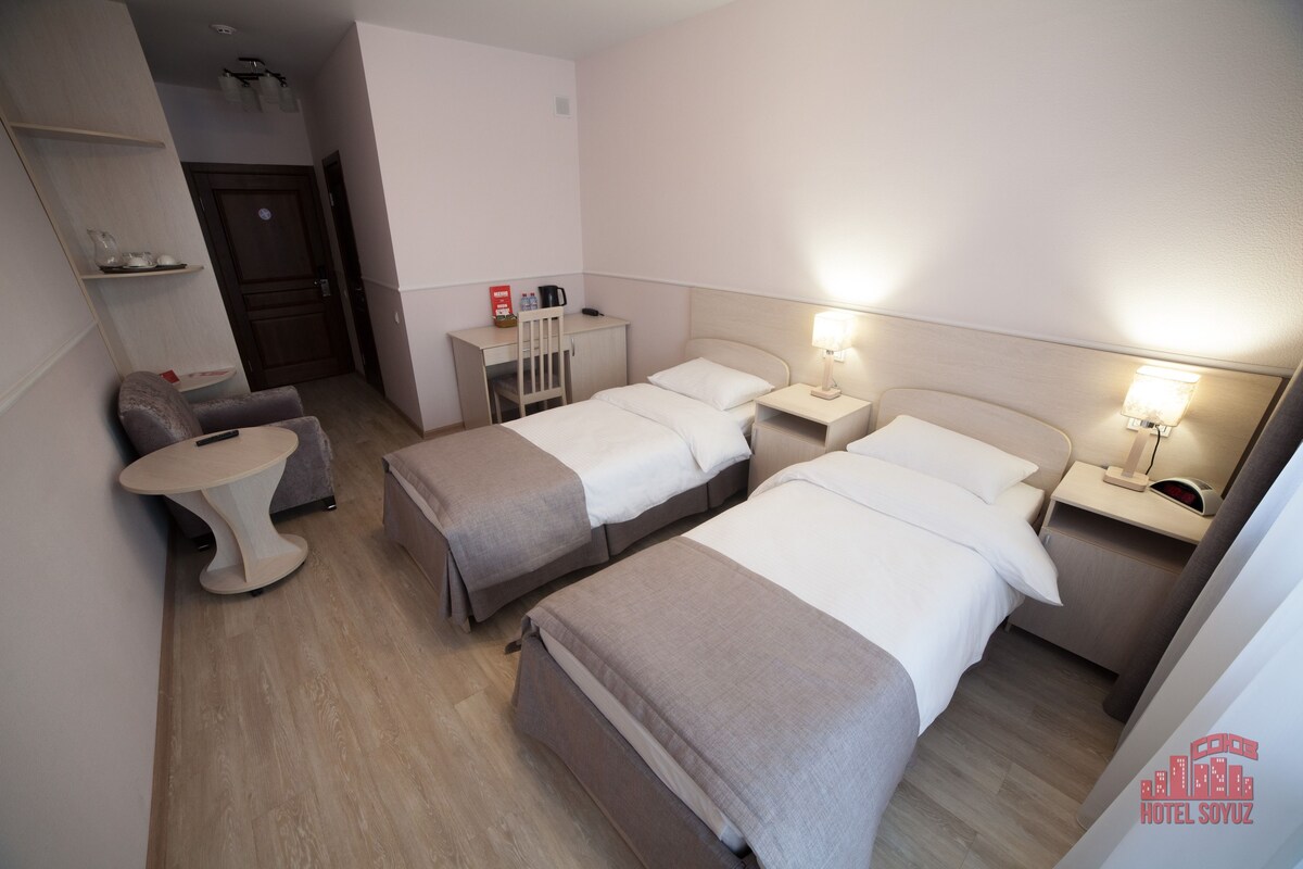 A hotel room with two beds, a desk, a chair, and a small table.