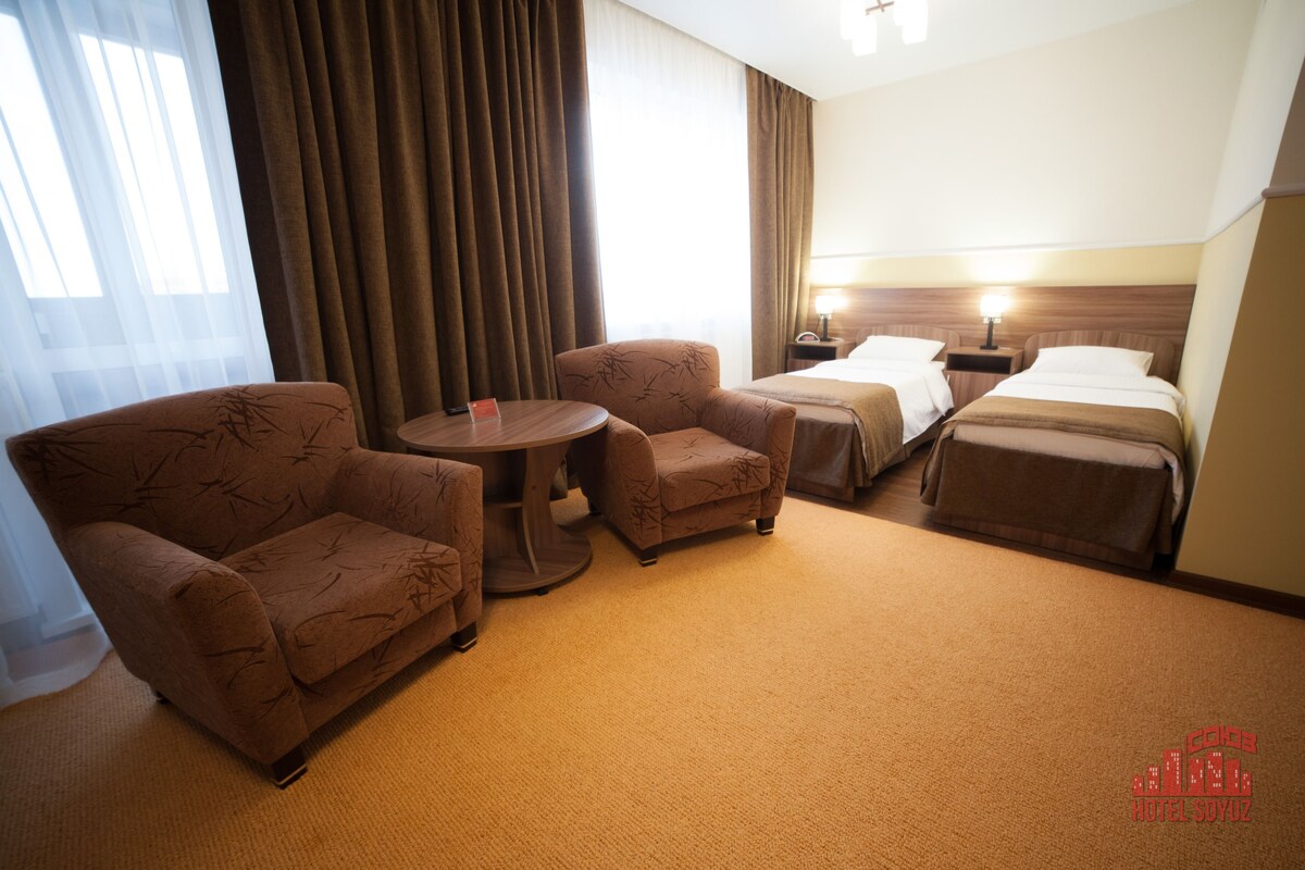 A hotel room with two single beds, a sofa, a small table, and a lamp.