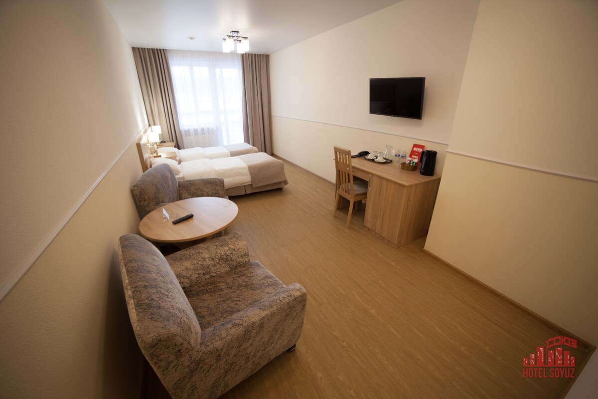 A hotel room with a bed, a desk, a chair, a sofa, and a TV.
