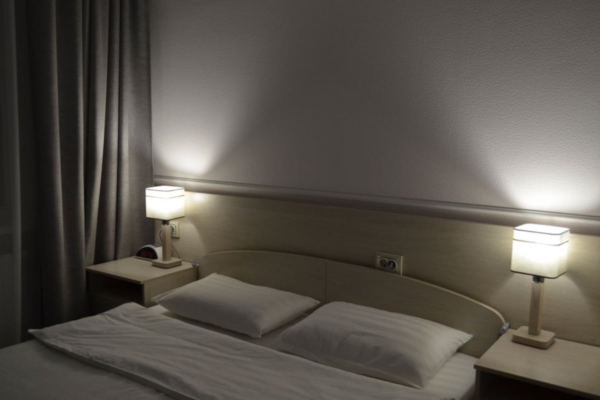 A hotel room with a bed, two bedside tables, and two lamps.