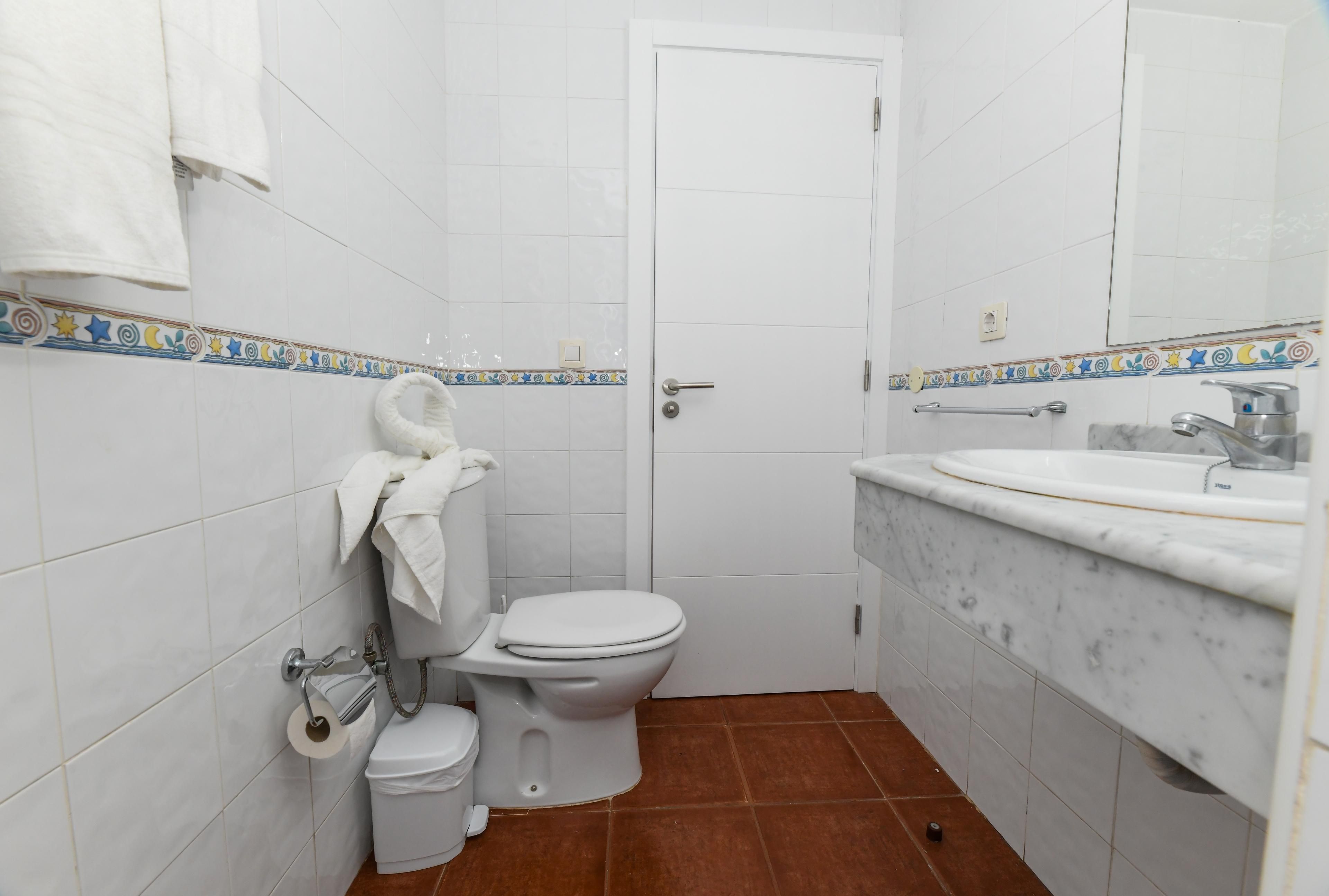 Ein kleines, sauberes Badezimmer mit weißen Fliesen, einer Toilette, einem Waschbecken mit Marmorplatte und einer Tür, an der ein Handtuch hängt.