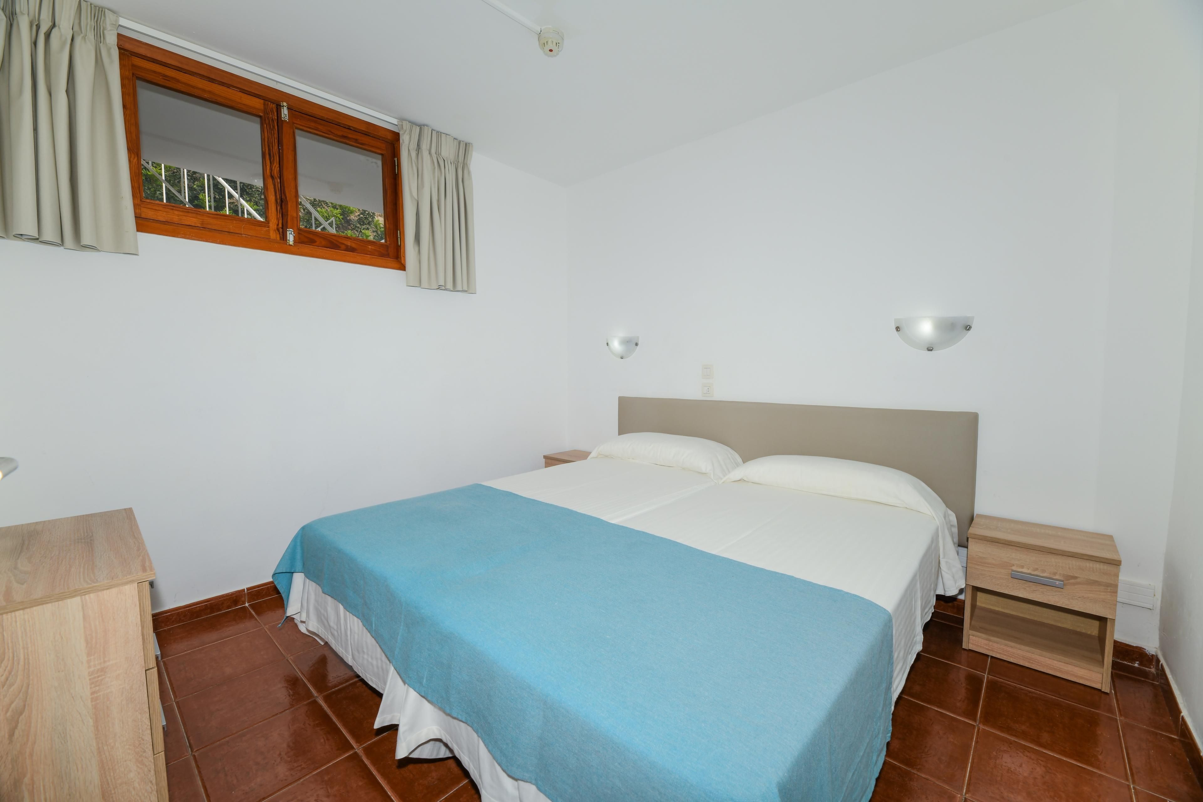 Una camera da letto con un letto, un comodino, una lampada da comodino, una finestra con tende e una luce a soffitto.