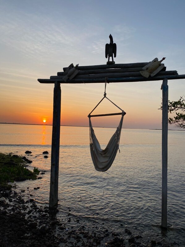 A hammock hanging from a wooden structure by a body of water during sunset. - Dakosta Eco Retreat (Bubaque)