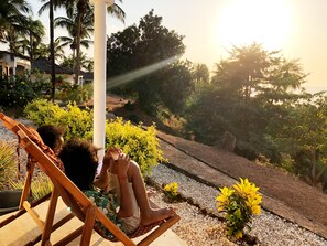 A person sitting on a wooden chair in a garden with a view of a beach and palm trees. - Dakosta Eco Retreat (Bubaque)