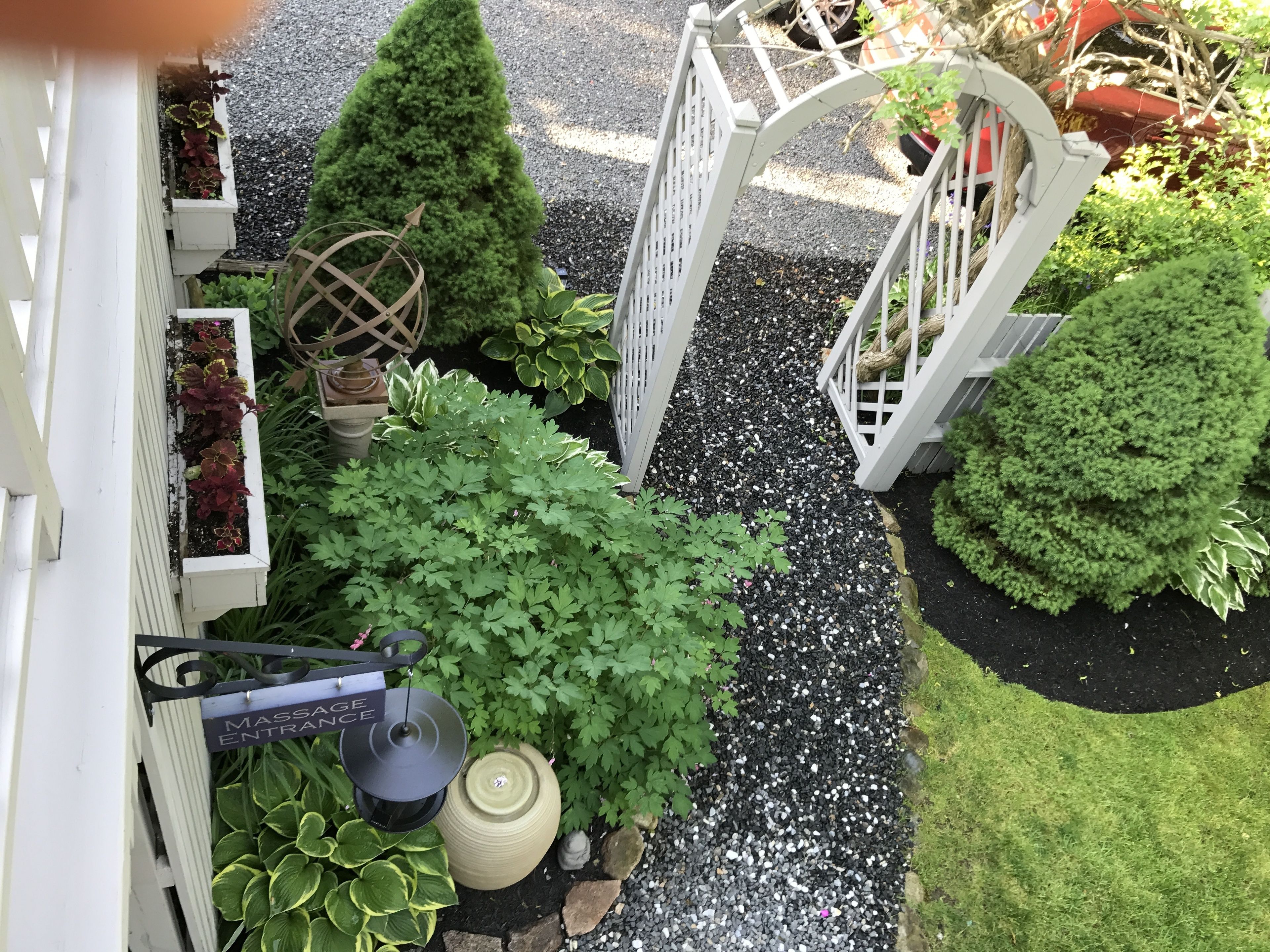 A garden pathway leading to a white gate, surrounded by various potted plants and a large decorative urn.