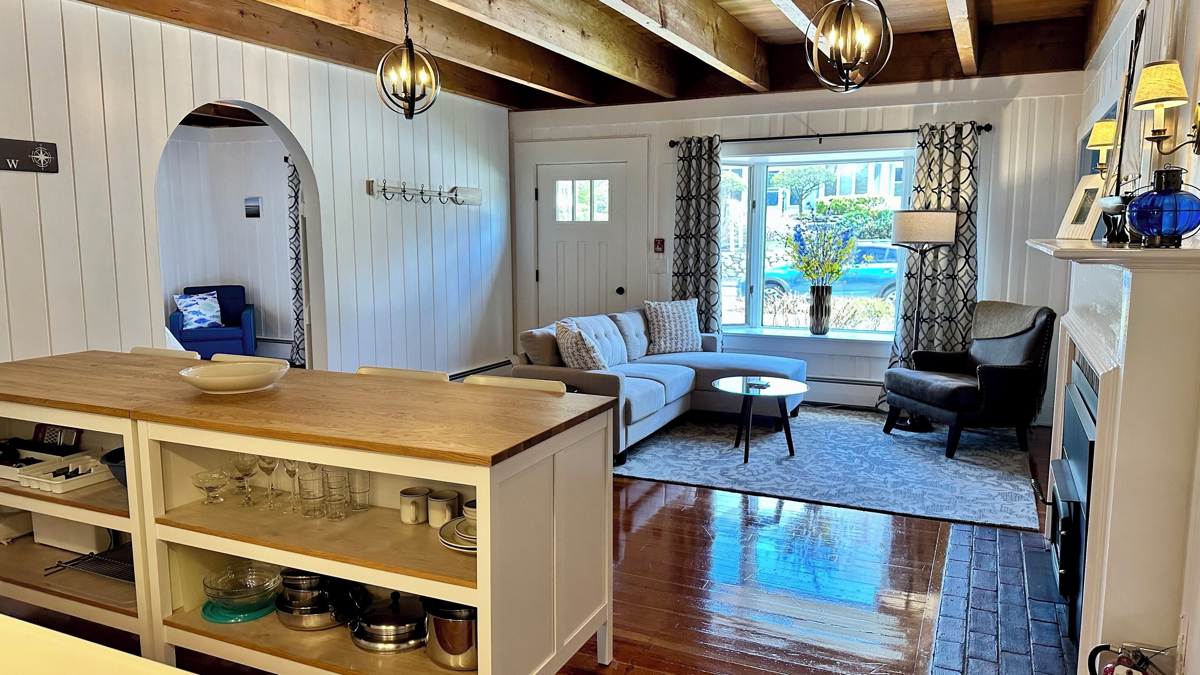 Ein gemütliches Wohnzimmer mit einem Holzesstisch, einer Couch und einem Couchtisch. Ein Fenster mit Vorhängen bietet Blick ins Freie.