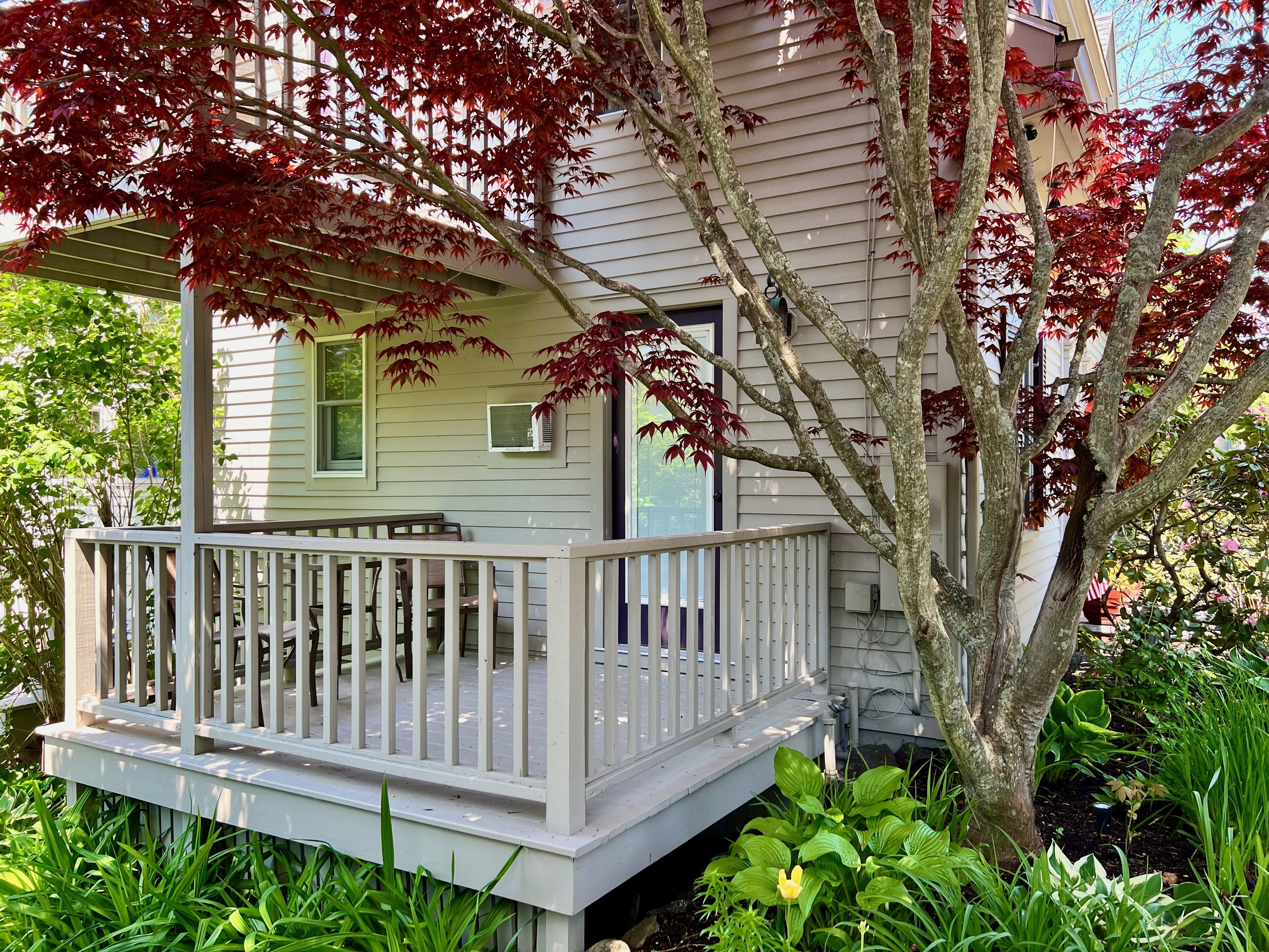 A house with a covered porch, a small deck, and a garden with various plants.