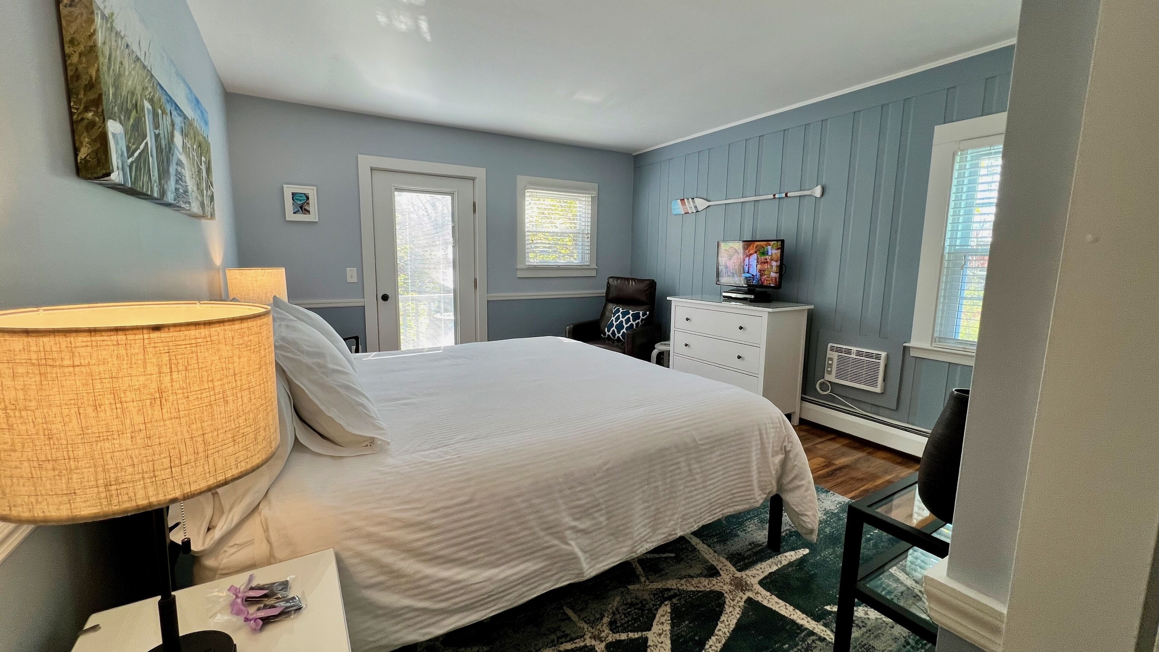 Un dormitorio con cama, televisión, silla, cómoda y ventana con persianas.