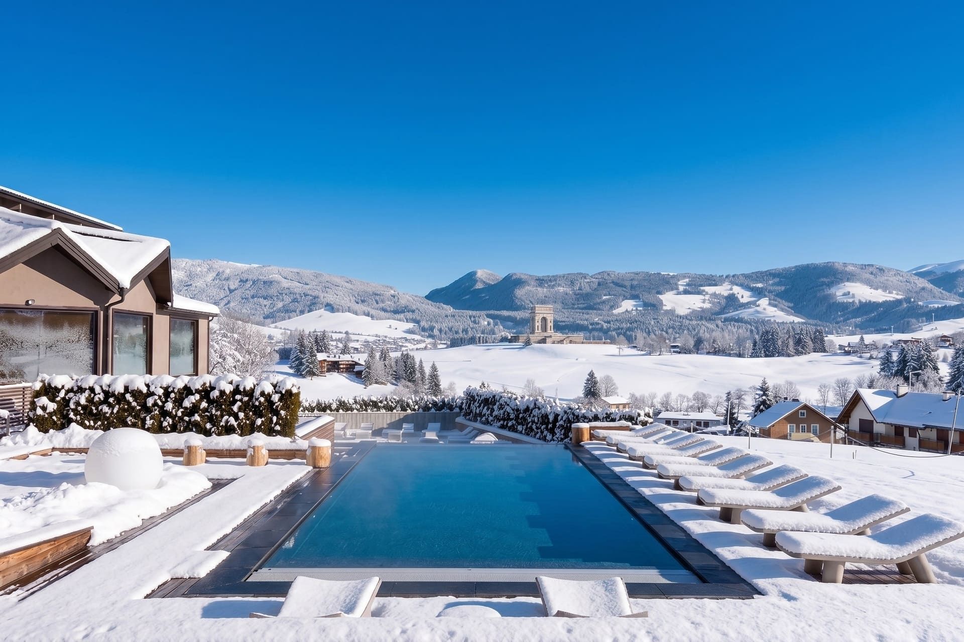 A snow-covered pool area with lounge chairs and a clear view of mountains.