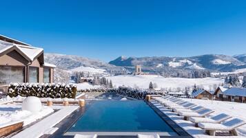 A snow-covered pool area with lounge chairs and a clear view of mountains.