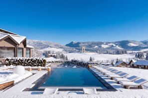 Un espace piscine enneigé, doté de chaises longues et offrant une vue dégagée sur les montagnes.