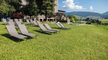 A hotel with outdoor lounge chairs, a pool, and a view of mountains.