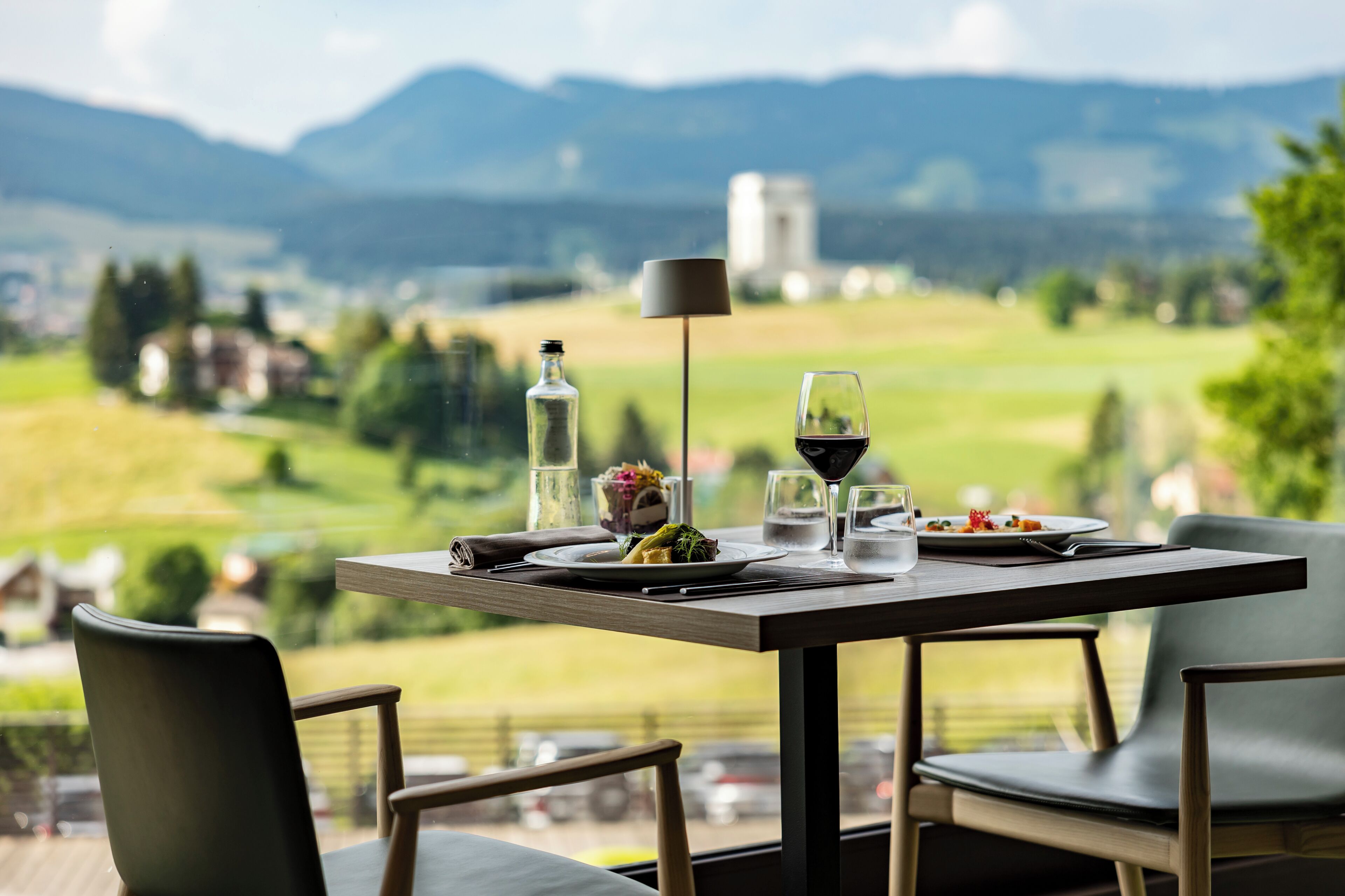 Een eettafel met borden, glazen en een fles, met een mooi berglandschap op de achtergrond.