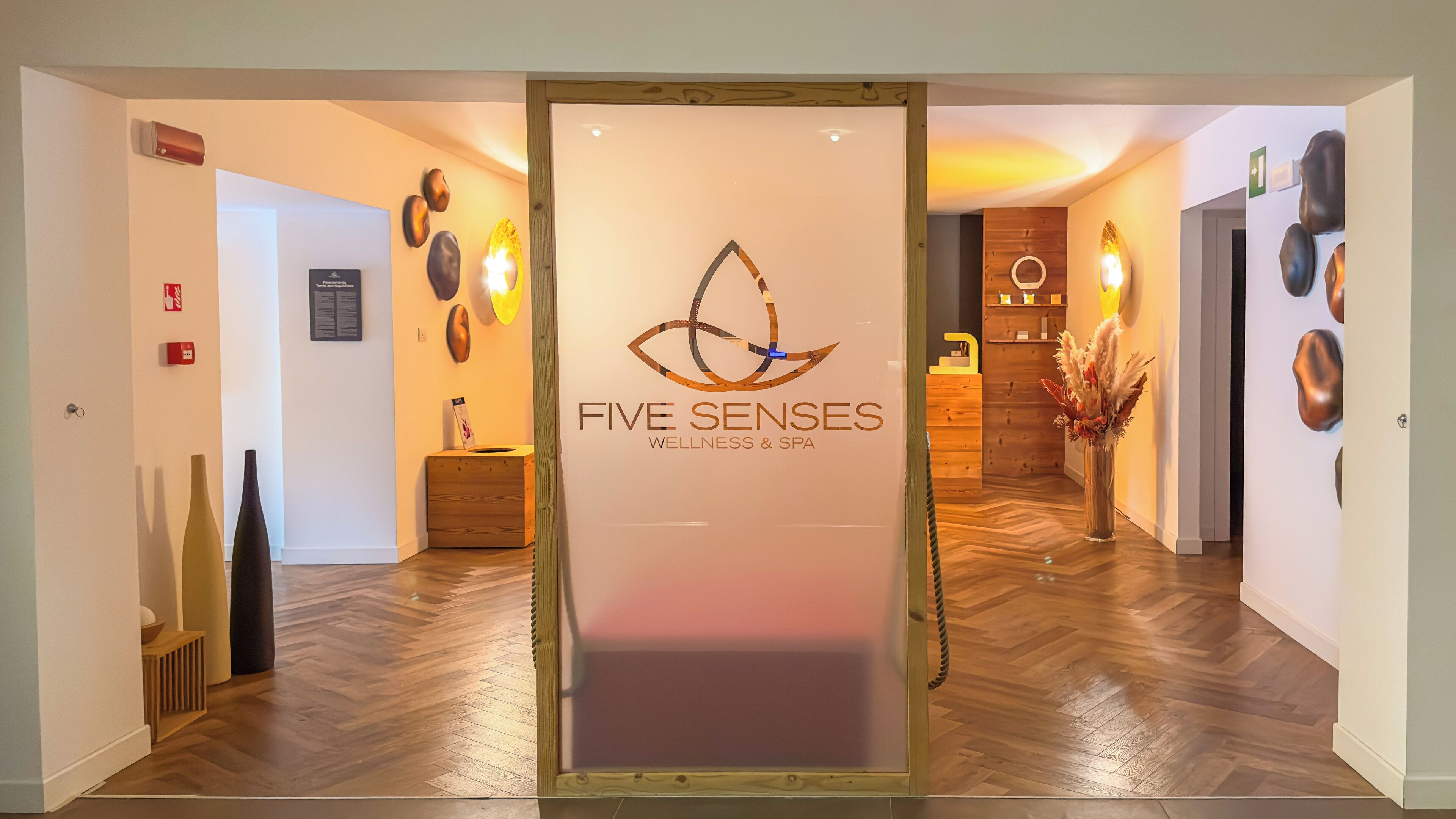 A reception area with a logo for 'Five Senses Wellness & Spa' and a wooden reception desk.