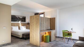 A modern hotel room with a bed, a wooden partition, a green chair, a small table, and a painting on the wall.