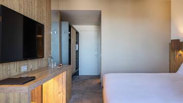 Ein modernes Hotelzimmer mit Schreibtisch aus Holz, einem Flachbildfernseher, einem Bett und einem begehbaren Kleiderschrank.