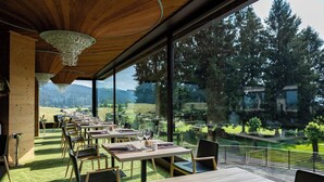 Un restaurante con mesas y sillas de madera, amplios ventanales con vistas a un paisaje boscoso.
