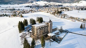 Un hotel grande con varios pisos y un patio central, rodeado de campos nevados y montañas al fondo.