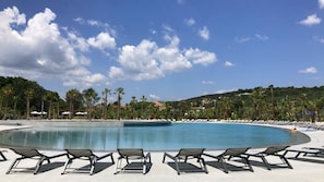 A large swimming pool with lounge chairs and umbrellas, surrounded by palm trees and a hilly landscape. - Dsone Vacances (Grimaud)