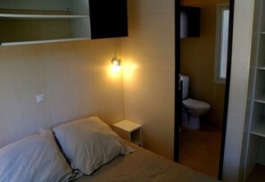 A small, dimly lit room with a single bed, a bedside table, a wall-mounted light, and a toilet. - Dsone Vacances (Grimaud)