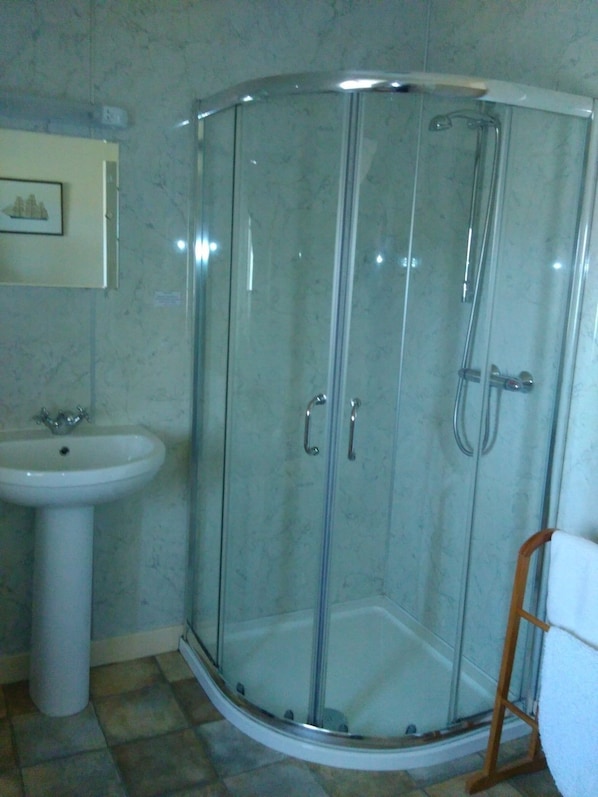 A corner shower with glass doors, a pedestal sink, and a wooden chair. - Strathy Inn (Thurso)