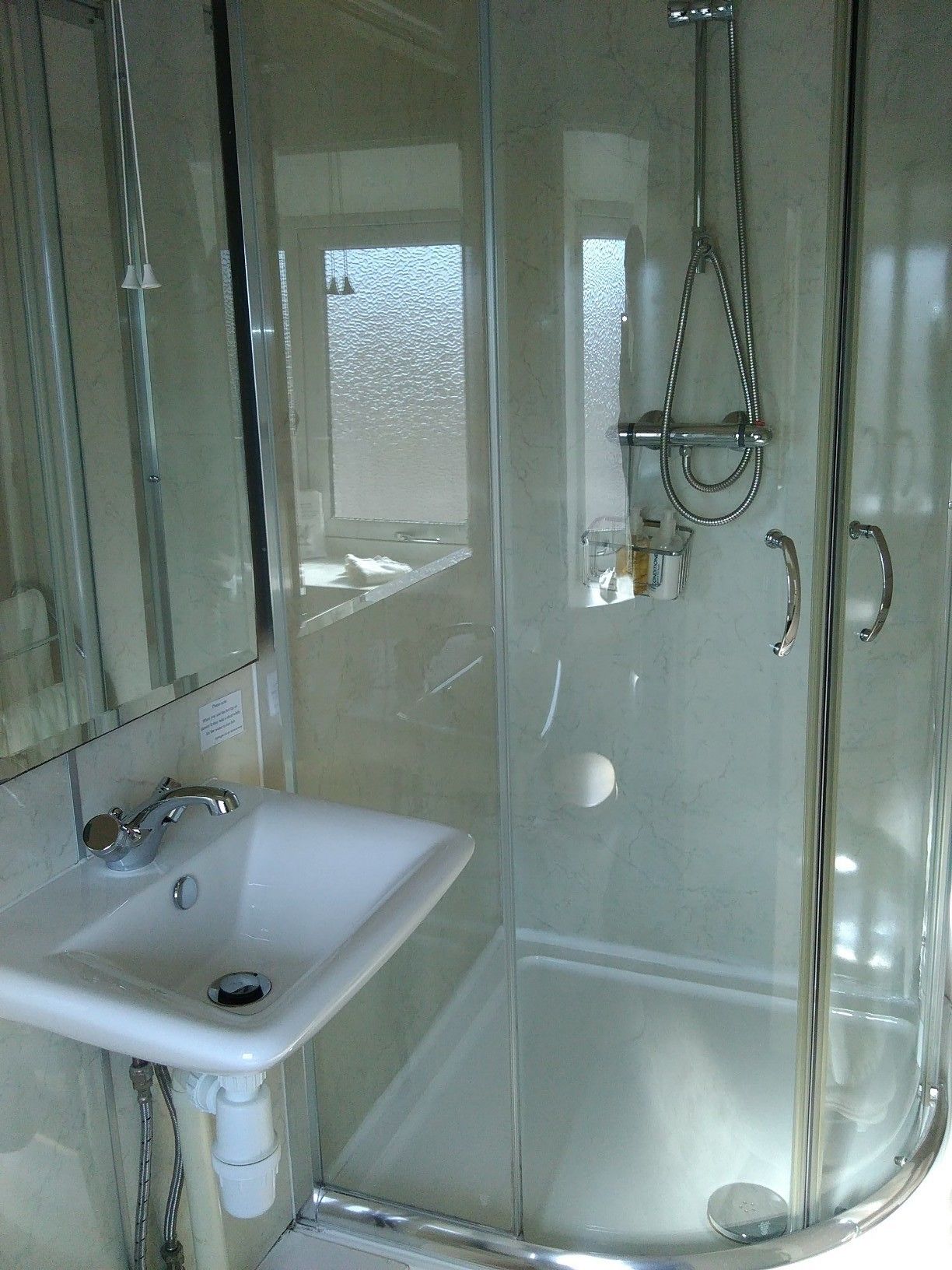 A glass-enclosed shower with a handheld showerhead and a handheld faucet.