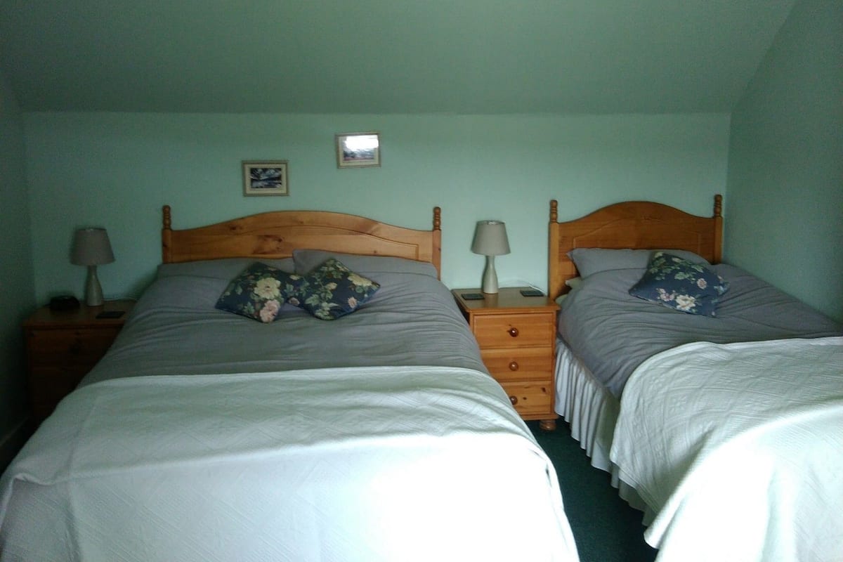 A twin room with two beds, each with a wooden headboard, a nightstand with a lamp, and a small drawer.