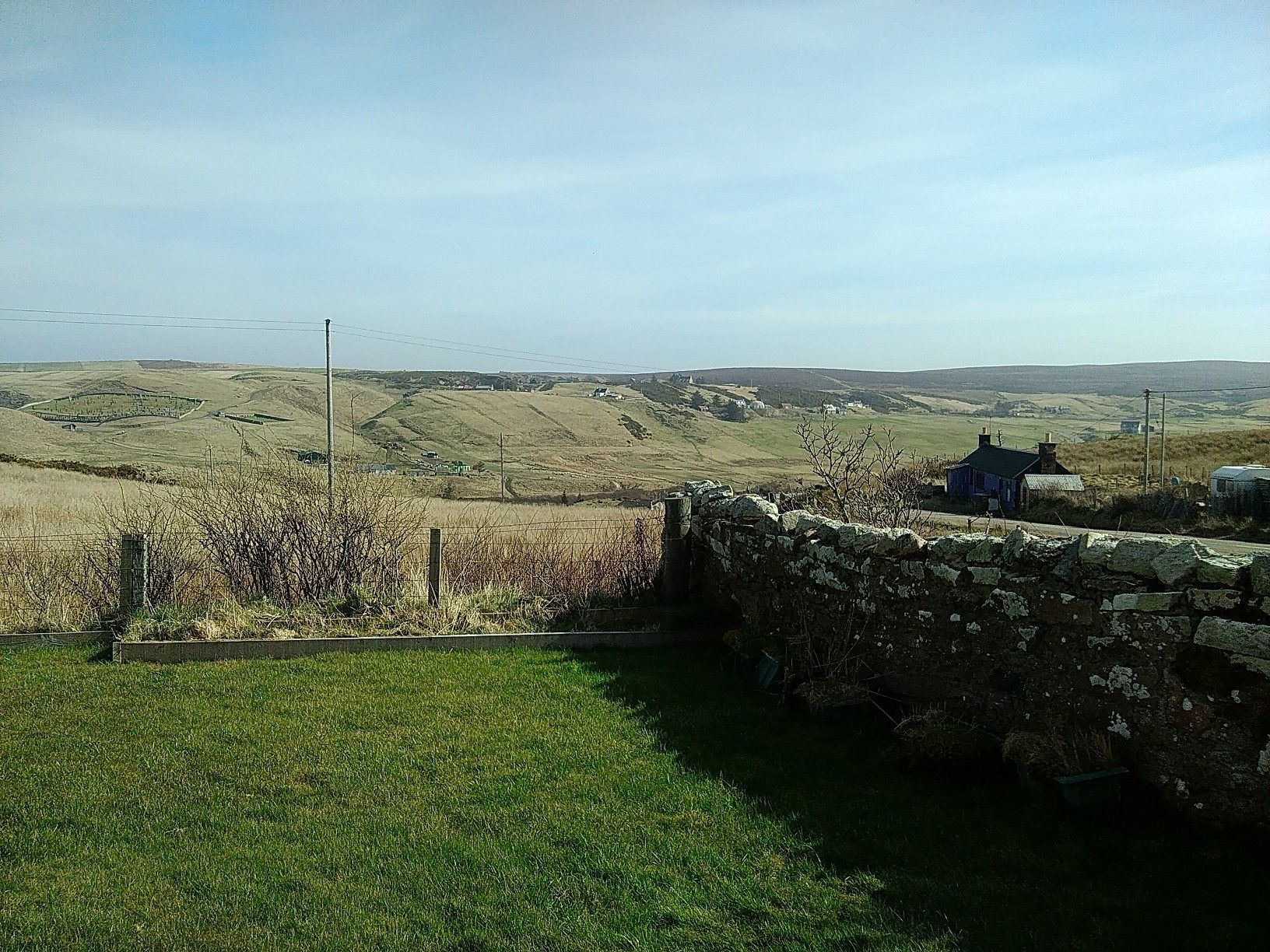 A rural landscape with rolling hills, a stone wall, and a small blue house.