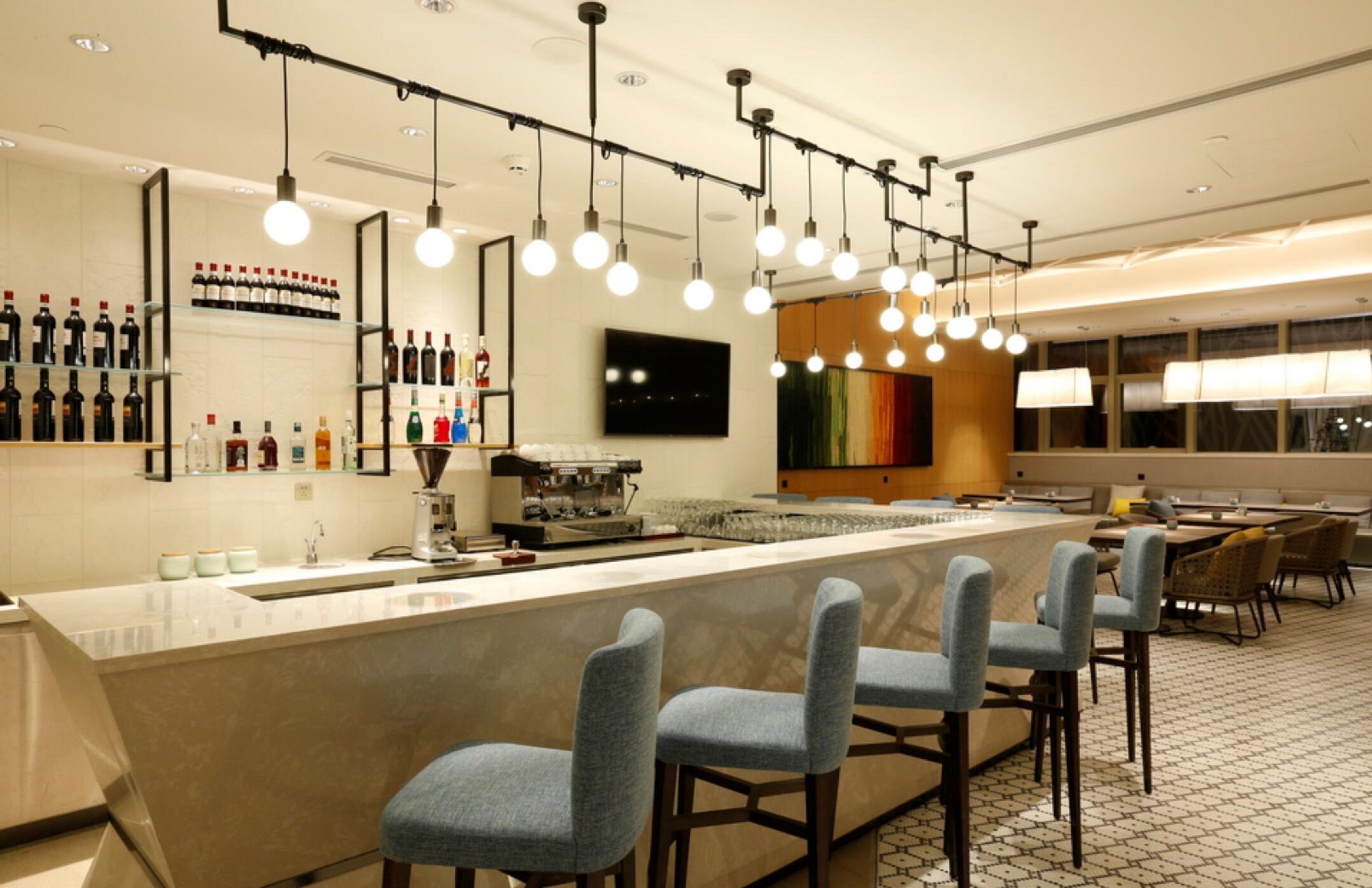 A modern bar area with a long counter, bar stools, and a variety of bottles on shelves.