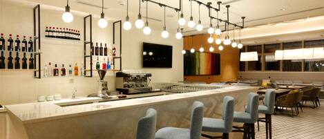 A modern bar area with a long counter, bar stools, and a variety of bottles on shelves.