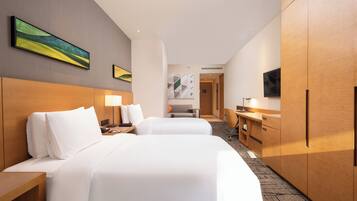 Habitación de hotel con dos camas, un escritorio, una silla, un televisor y obras de arte en las paredes.