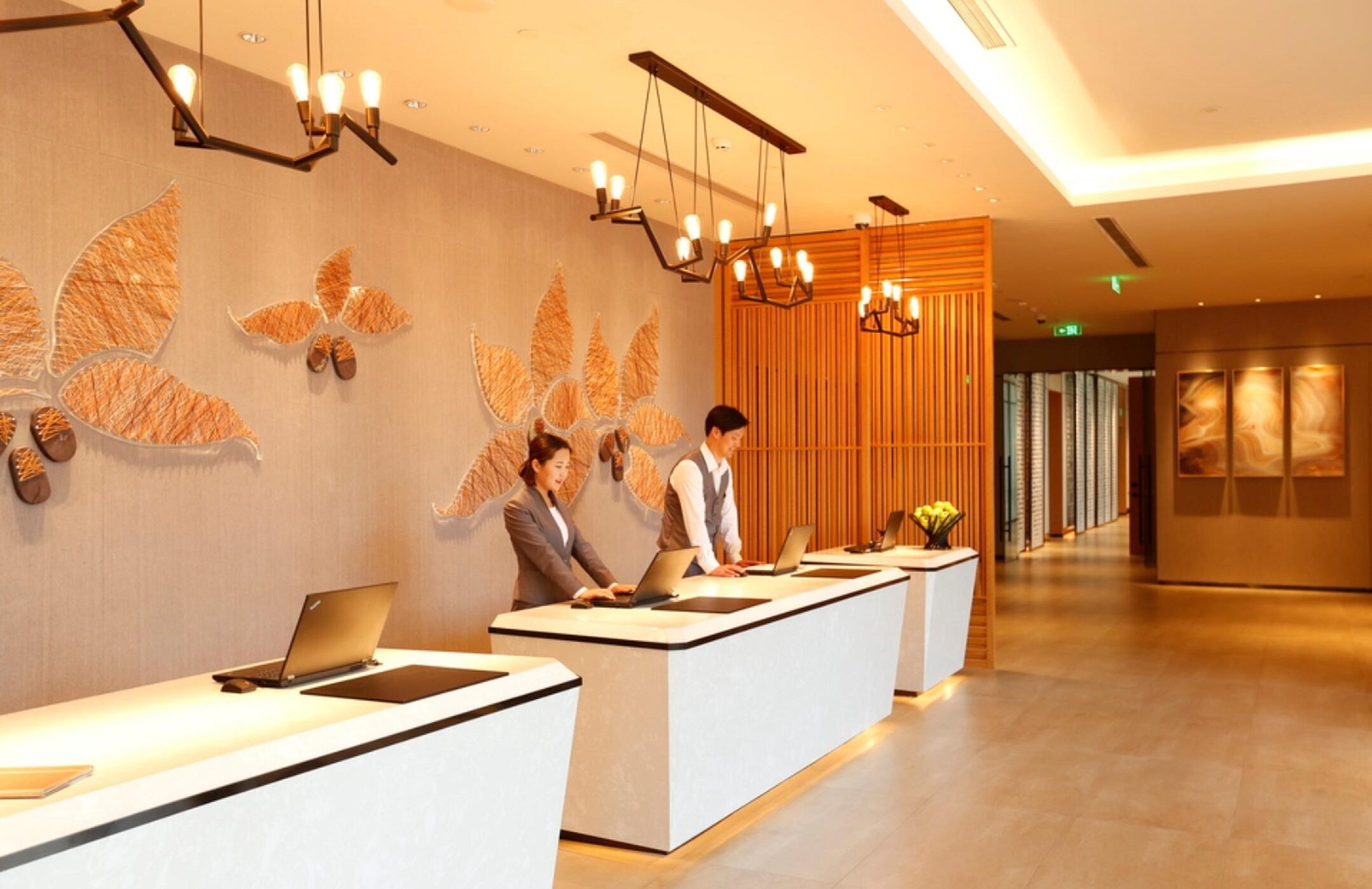 A reception area with a modern design, featuring a long reception desk, a decorative wall with leaf patterns, and a contemporary chandelier.
