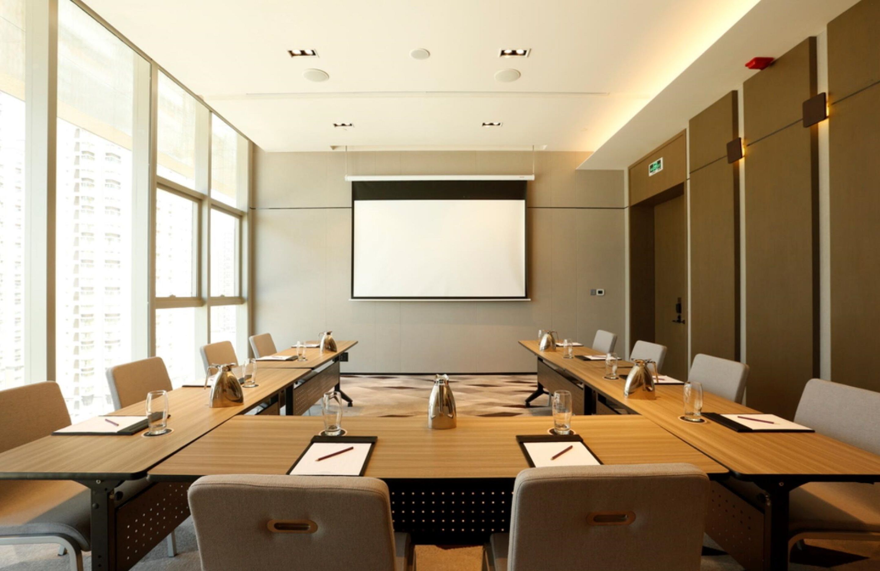 A conference room with a large screen, long tables, and chairs.