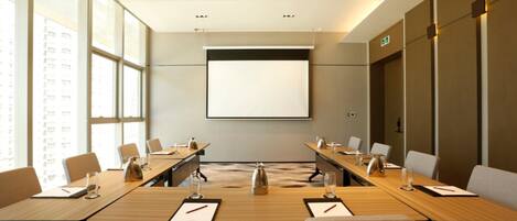 A conference room with a large screen, long tables, and chairs.