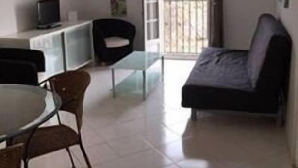 Una habitación con cama, una mesa de comedor con sillas, televisión y balcón.