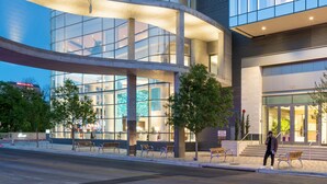 Un bâtiment moderne doté d’une façade en verre incurvé, d’un espace extérieur aménagé pour s’asseoir et offrant une vue dégagée sur l’intérieur.