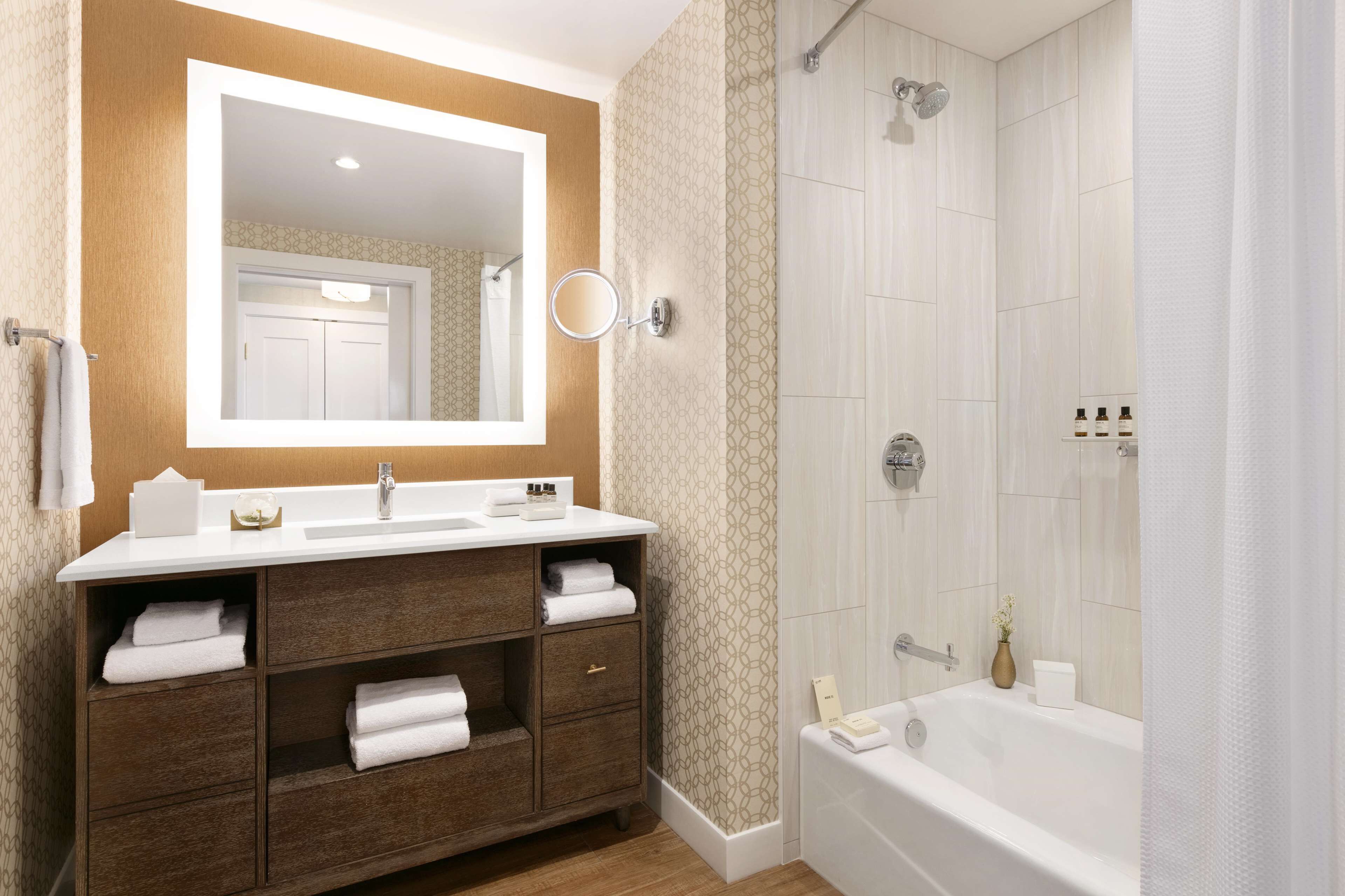 A modern bathroom with a large mirror, a sink, a vanity with drawers, a bathtub, and a shower.
