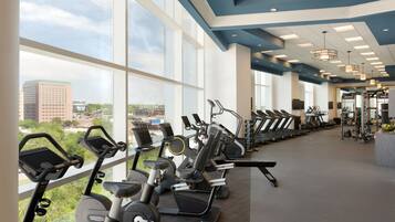 A gym with cardio machines, weightlifting equipment, and large windows offering a city view.